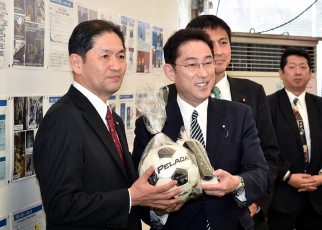 Minister Kishida holds a football ball and other items presented to him