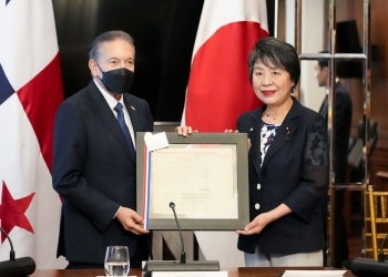 President Cortizo and Minister Kamikawa hold up a gift side by side in front of the flags of both countries