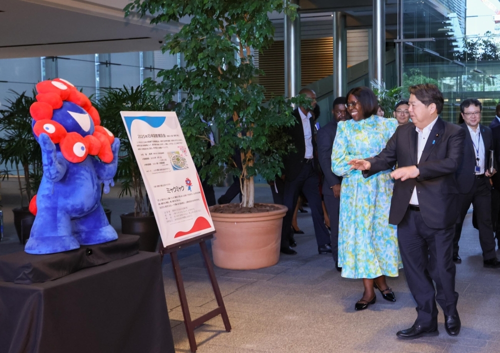 Chief Cabinet Secretary Hayashi and H.E. Ms. LEVI, Prime Minister of Mozambique, smile in front of the Expo 2025 Osaka character ”Myakumyaku-kun”