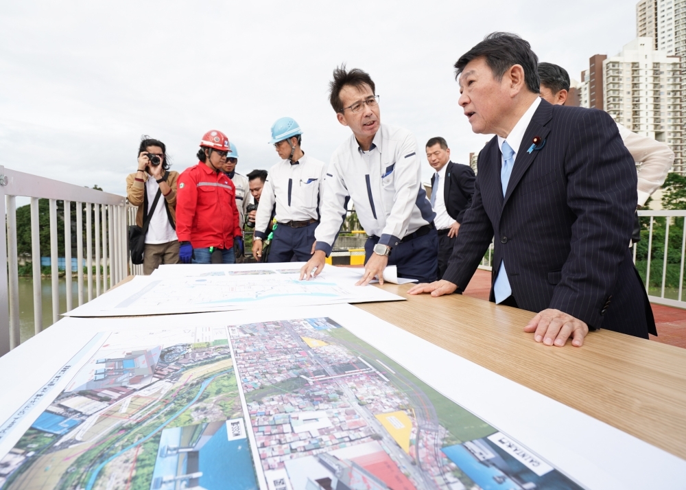 Minister Motegi hearing the explanation of the staff of the project in front of the photo of the site