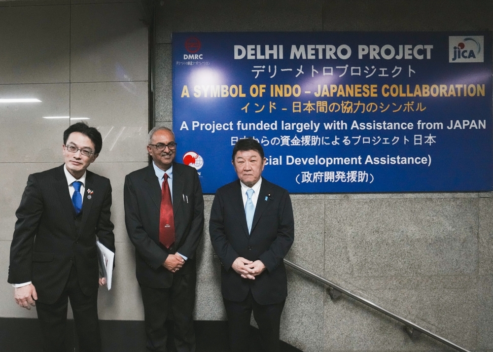 Foreign Minister Motegi in front of a sign for the Japanese Government Development Assistance Delhi Metro Project