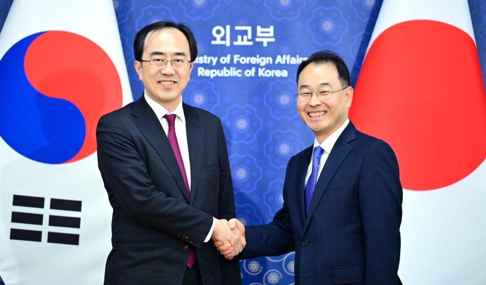 Senior Deputy Minister AKAHORI  shaking hands with Deputy Minister for Economic Affairs PARK Jong Han in front of the national flags