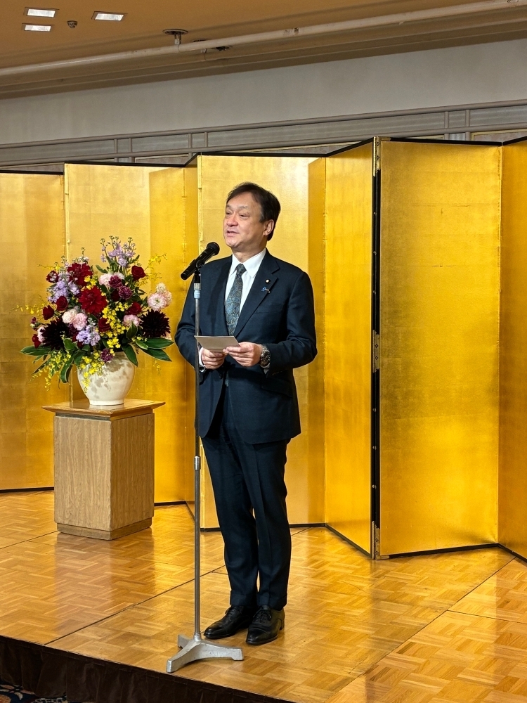 State Minister HORII delivering remarks as the host in front of the gold folding screen