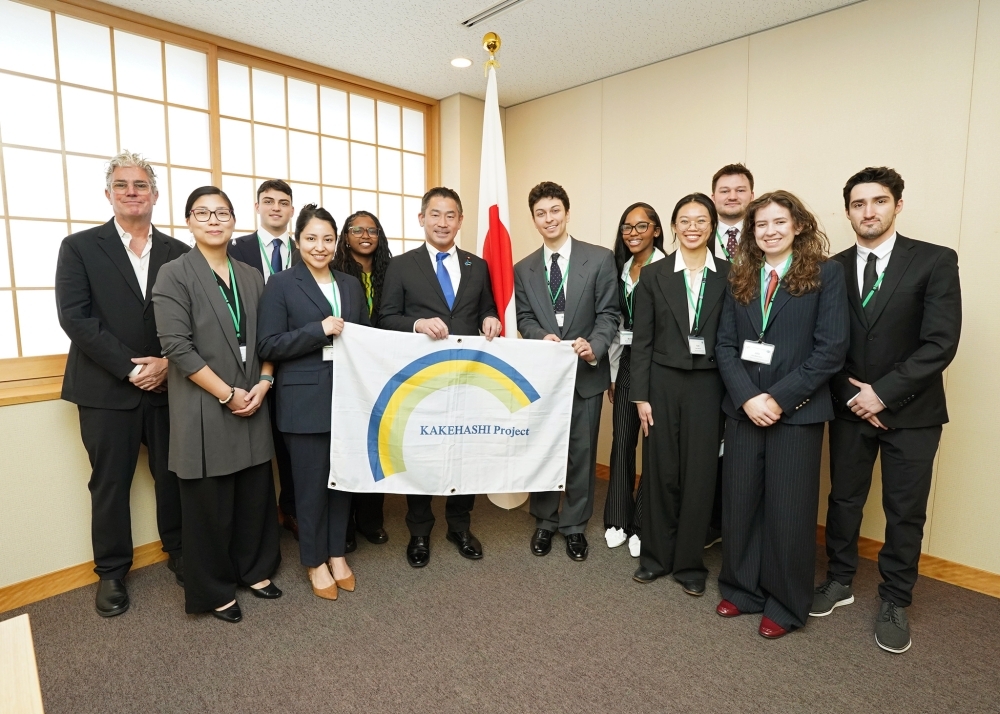 Group photo showing Parliamentary Vice-Minister ONISHI and two members holding the “Kakehashi Project” banner, with the rest of the Inoue Program delegation lined up alongside them