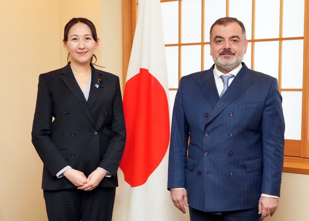 Parliamentary Vice-Minister Eri and Ambassador Talibov pose for a photo in front of the Japanese flag