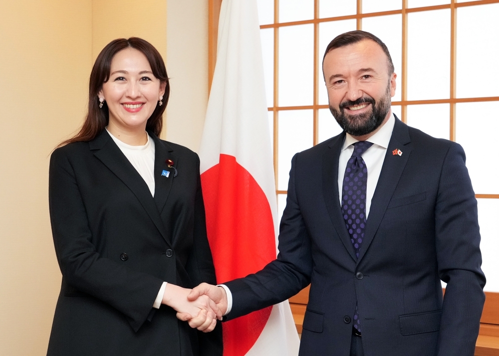 Parliamentary Vice-Minister ERI and Ambassador Muça shaking hands in front of the Japanese fla