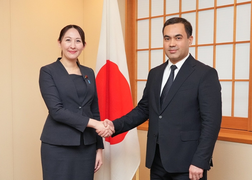 Parliamentary Vice-Minister ERI shaking hands with Deputy Minister ABDULLAEV in front of the Japanese national flag