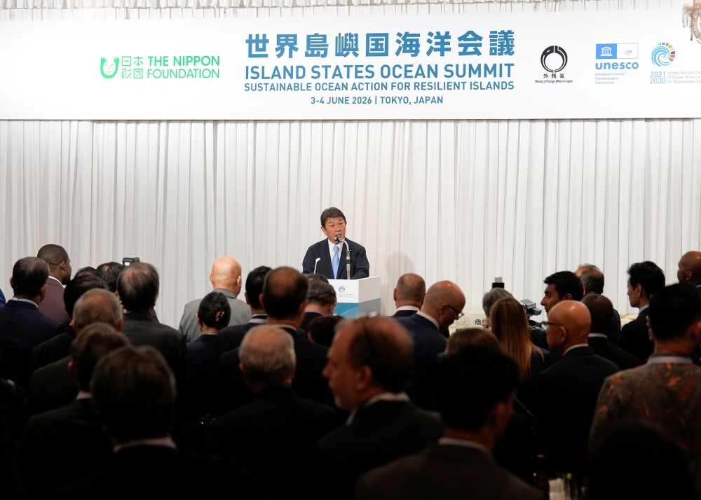Minister Motegi delivering remarks from the stage at the reception venue, with the attendees