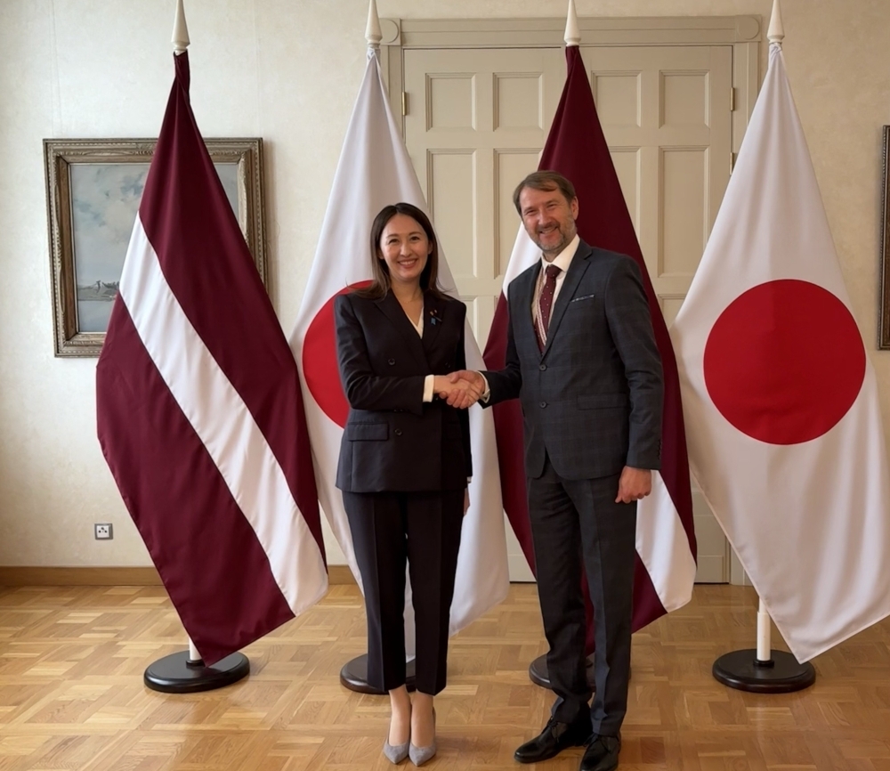 Parliamentary Vice-Minister ERI shaking hands with Mr. Andžejs Viļumsons, State Secretary, Ministry of Foreign Affairs of Latvia, in front of the flags of both countries