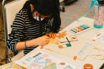 (写真1)エコバックの真ん中にアイルランドと日本の国旗、その下に熊や鹿の絵を描く子供の様子