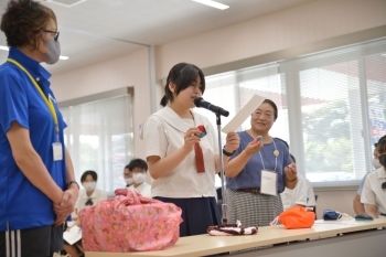 (写真1)市民手作りのおみやげを選手団に英語で説明する仁賀保高校の生徒さん