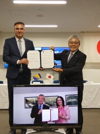 (写真2)協定書を披露するすさみ町長(後方右)とイェゼロ市長(画面内右)署名に立ち会ったベリャン大使(後方左)と伊藤大使(画面内左)