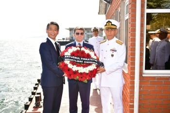 トルコ関係者と共に献花用の花輪を持ち、記念撮影に応じる、山田副大臣の様子