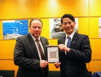 ウクライナの郵便局発行の記念切手を持ち、記念撮影に応じる、山田副大臣とコルスンスキー大使の様子