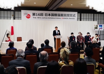 演台に立ちスピーチする武井副大臣、およびステージ上で着席してスピーチを聞く受賞者の様子