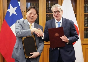 協定書への署名後に、正面を向き、笑顔で握手を交わす、両大臣の様子