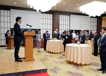 挨拶する穂坂外務大臣政務官と、会場の出席者の様子
