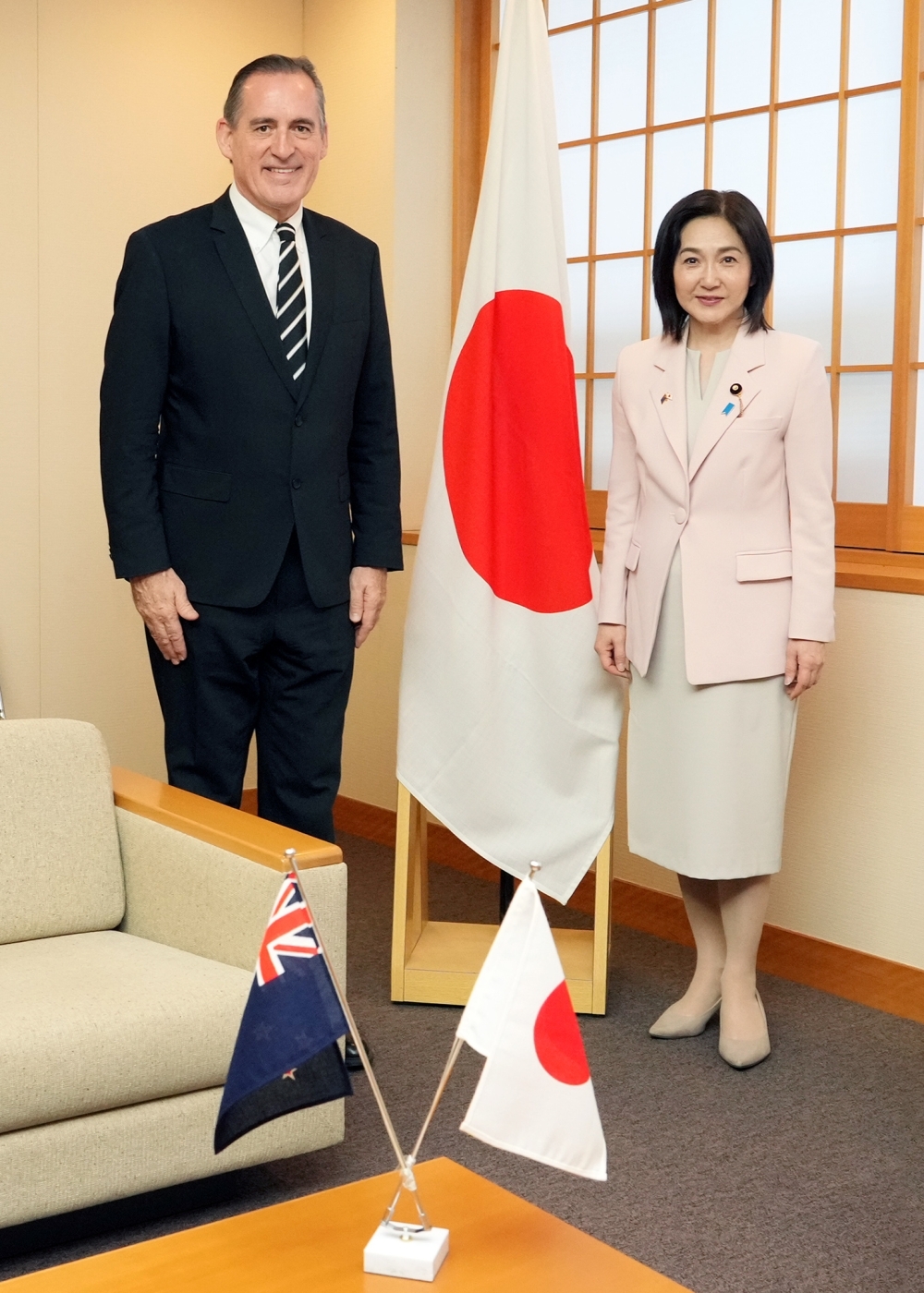 日本国旗の前で写真撮影するクーパー大使と生稲外務大臣政務官