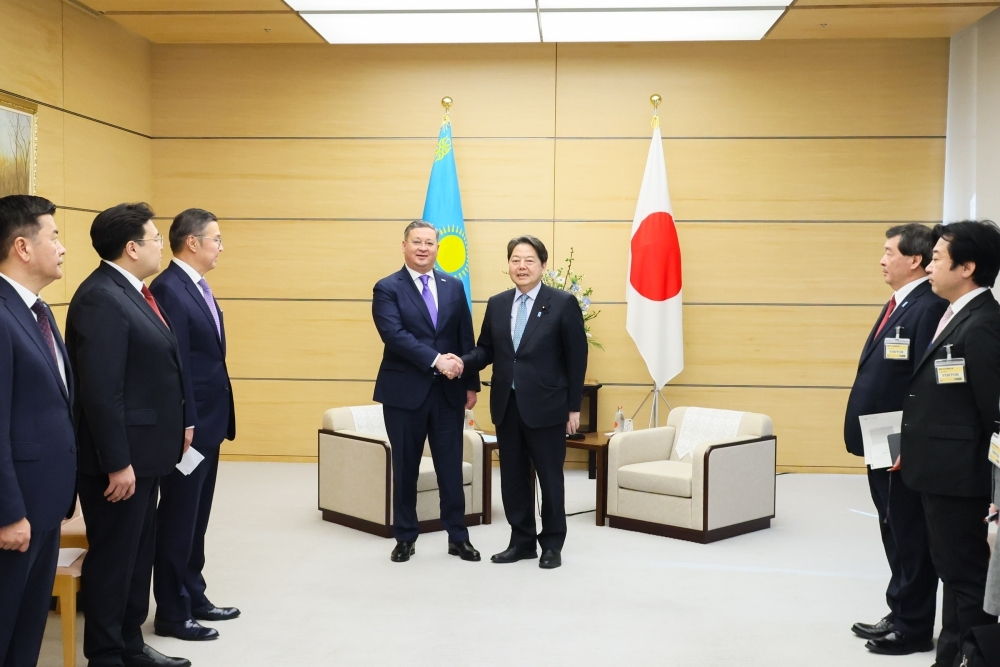 両国の国旗前で握手をする林官房長官とカザフスタン共和国副首相兼外務大臣の様子