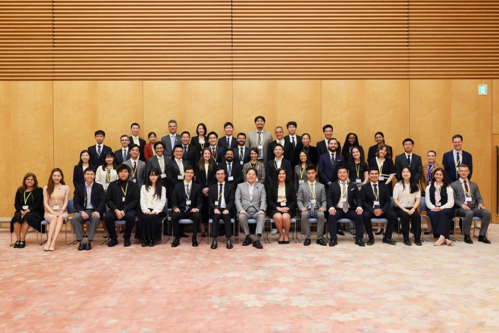 4列横並びになった学生一行と記念撮影する林官房長官の様子