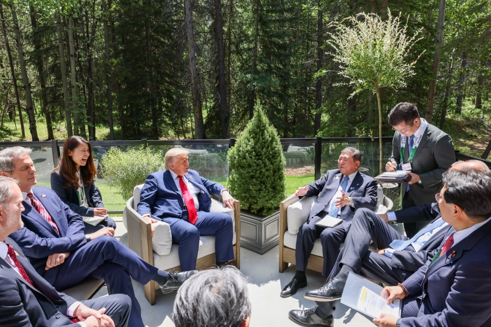 屋外で椅子に座り会談する石破総理大臣とトランプ米国大統領。周りに両国の関係閣僚も同席。