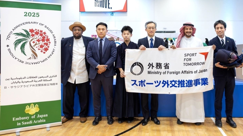 外務省スポーツ外交推進事業の旗を持つ森野泰成駐サウジアラビア大使と事務総長、その他関係者の方々との記念写真の様子
