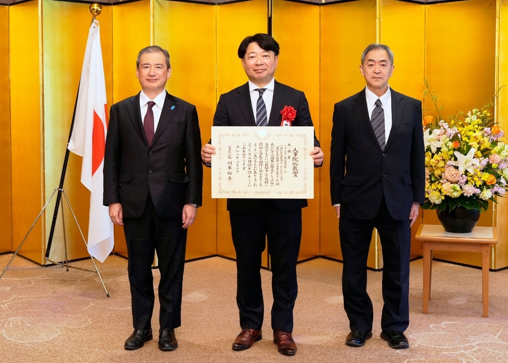 金屏風の前で、賞状を手に撮影に応じる外務省のミャンマー地震対応チーム代表