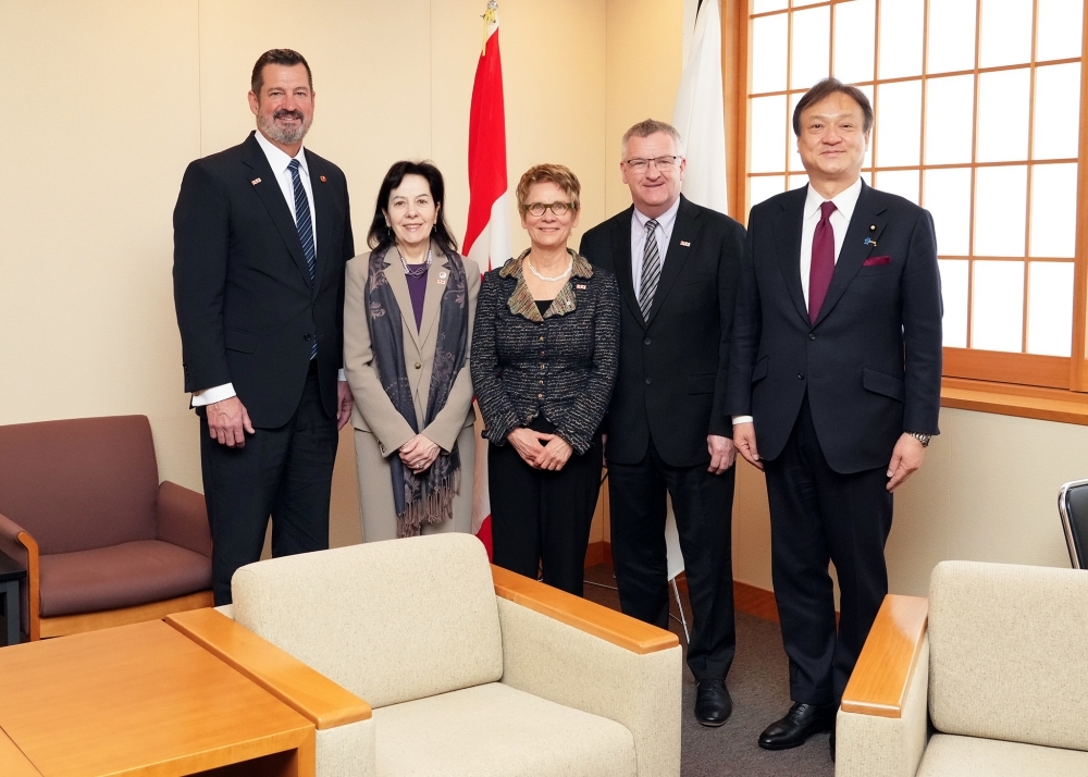 日本国旗の前に立つ堀井副大臣の左手側にガニエ上院議長とマニング上院議員、サン＝ジェルマン上院議員、ダンカン・ウィルソン氏が並んだ記念写真