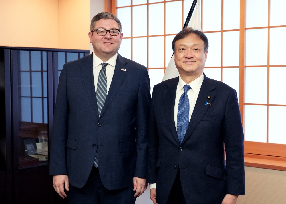 日本国旗の前に立ち撮影に応じる堀井副大臣とヴェンホイズン副知事