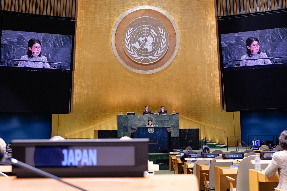 壇上で総理大臣メッセージの代読をする国光副大臣の姿が会場前面上方にある大型モニター2機に映されている様子