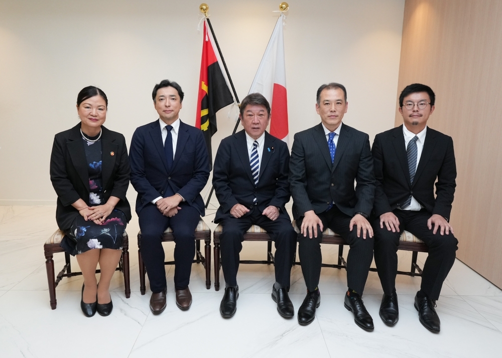 両国旗の前に座って、アンゴラ在留邦人（4名）と記念撮影する茂木外務大臣（中央）