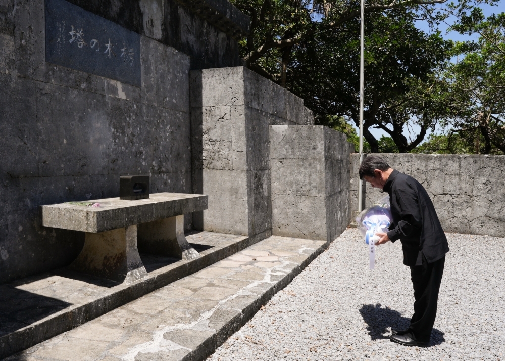 石碑の前で、茂木外務大臣が黒い正装姿で供花を両手に持ち、石造りの祭壇に向かって深々と頭を下げて哀悼の意を表している様子