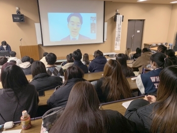 (写真)スクリーンに映し出された国際協力局地球規模課題総括課の小島拓磨課長補佐と東海学院大学の生徒さんたちの様子