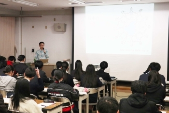 教室前方のスクリーンのそばで説明する中野講師。