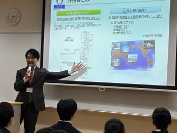 投影スクリーンの前で資料を背に説明する川崎講師。