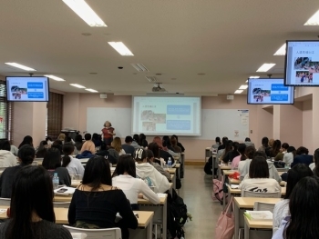 教室内で、前方の講師に注目しながら話を聞く学生たちの様子。