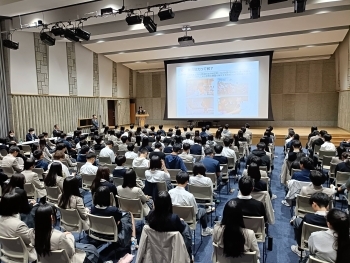大講堂で行われた講座の様子。スクリーン前に講師が立ち、生徒約100名以上が座席について講義を聞いている。