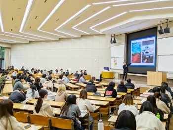 大学の大教室で、多くの学生が着席し、スクリーンに映された資料を見ながらODA出前講座を受講している様子。
