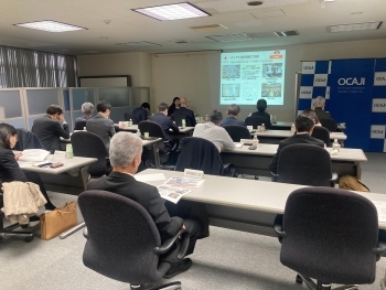 会議室で開催されたODA出前講座の様子。スクリーンを用いて説明を行う講師の話を参加者が資料を見ながら聴講している。