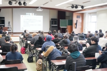 大学の講義室で、多くの学生がスクリーンを見ながらODA出前講座に参加している全体風景。