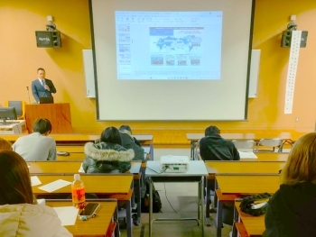 講師がスライドを用いて日本の開発協力について説明し、学生が資料を見ながら熱心に耳を傾けている様子。