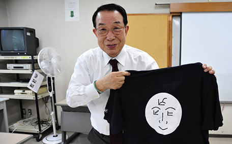 プロジェクトのマーク入りのシャツを手にする司馬さん。仏陀の「第3の眼」がデザイン化されている（写真：JICA）