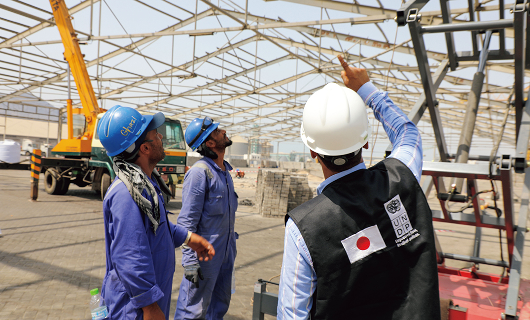 イエメンにおける無償資金協力「アデン港における効率性改善計画（UNDP連携）」において、貨物処理の迅速化を実現するため、港の貨物上屋の改修作業に従事するイエメン人作業員とUNDP職員（写真：UNDP）