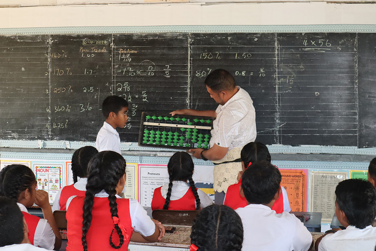 黒板の前でそろばんを持つ先生と生徒