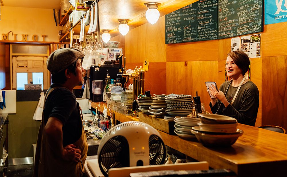 Rachel smiling and conversing with a bar owner while taking notes.