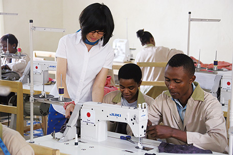 Ms. Yamahira (left) checks the work of trainees in front of an electric sewing machine for industrial use. There are several men among the trainees. (Photo: Yasuko Yamahira)