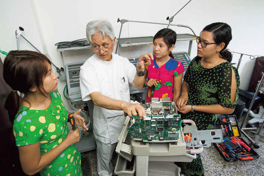 Senior Volunteer, Mr. Kyuzo Iwai providing support in the building of a system for the maintenance and management of medical equipment at the New Yangon General Hospital in Myanmar. Understanding of the structure is enhanced as he disassembles the equipment together with the personnel involved. (Photo: Shinichi Kuno / JICA)