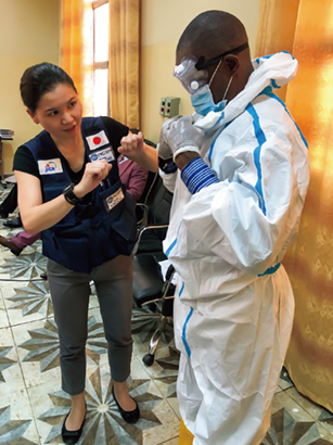 An infection control expert of the Japan Disaster Relief (JDR) Infectious Diseases Response Team providing instruction to a medical care worker on how to put on and remove protective clothing that protects against the Ebola virus in the Democratic Republic of the Congo (Photo: JICA)